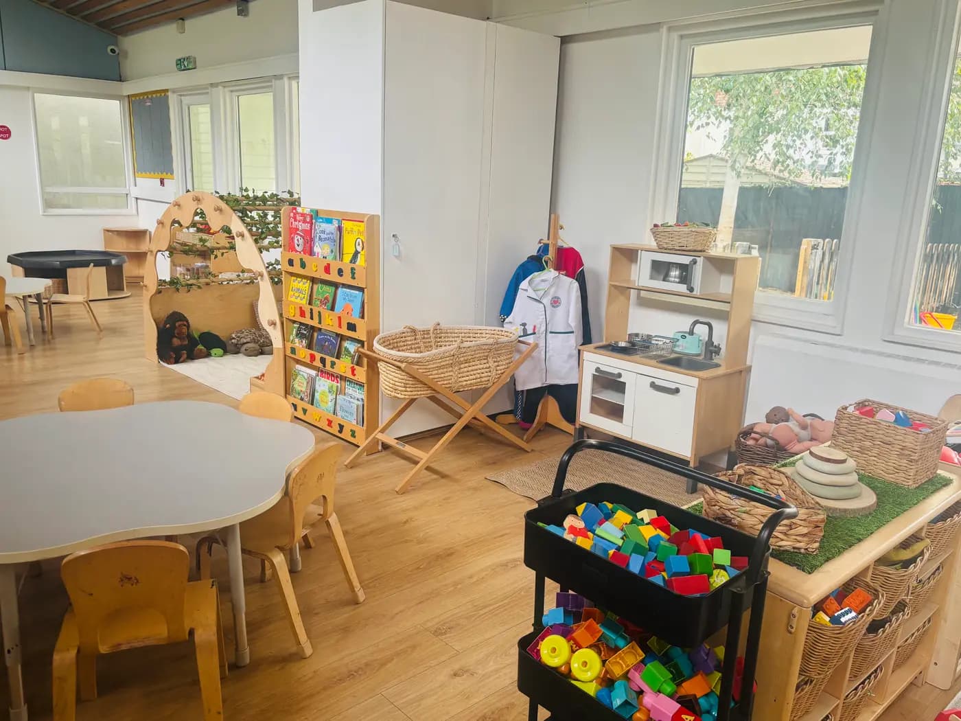 A bright nursery room with a play kitchen, bookshelves and baskets of resources