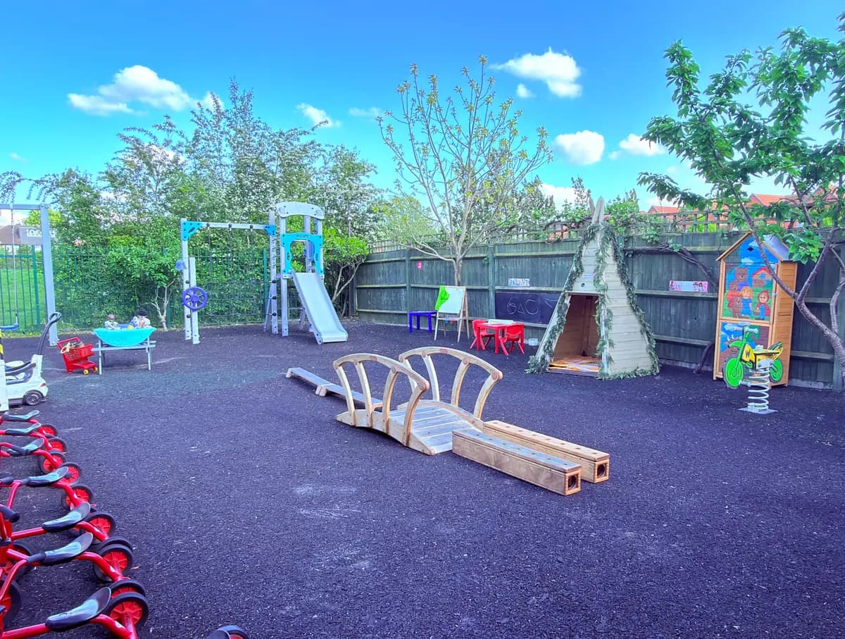 A sunny outdoor play area with a climbing frame, slide and wooden balance beams