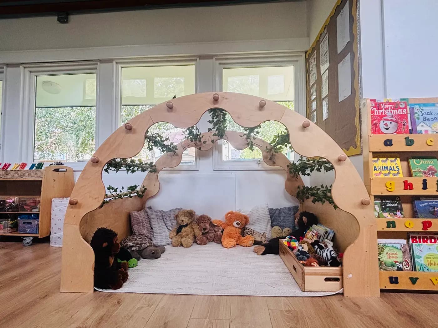 A cosy wooden reading nook with soft toys, cushions and picture books